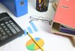 Actualisation des prix d'un marché public : calculatrice et tableaux de prix sur un bureau
